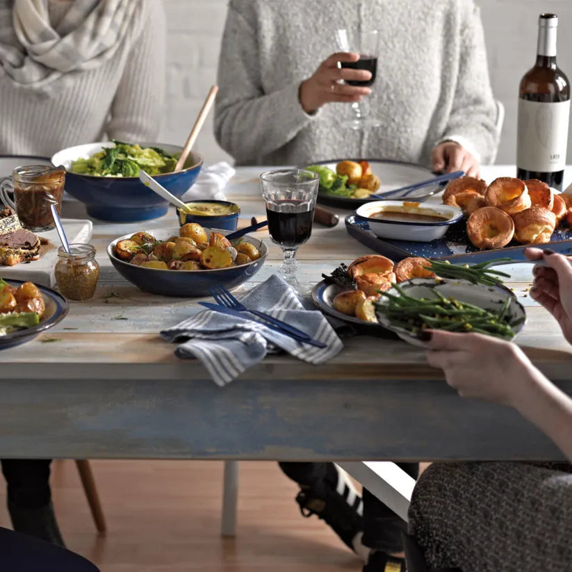 Denby Imperial Blue serving bowls filled with roasted potatoes and salad on a dining table during a meal.