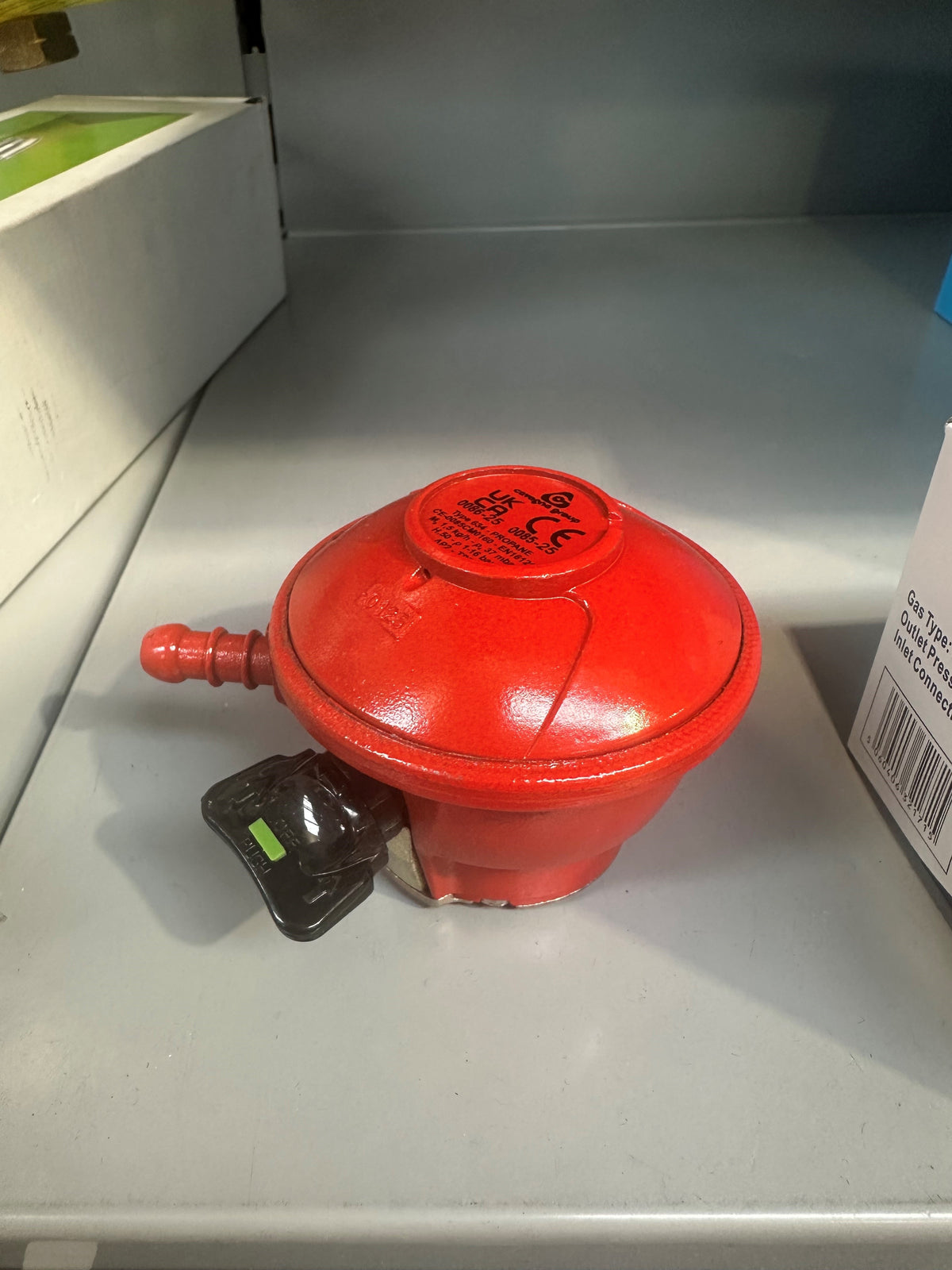 Red low pressure 27 mm patio gas regulator with black adjustment knob on gray shelf.