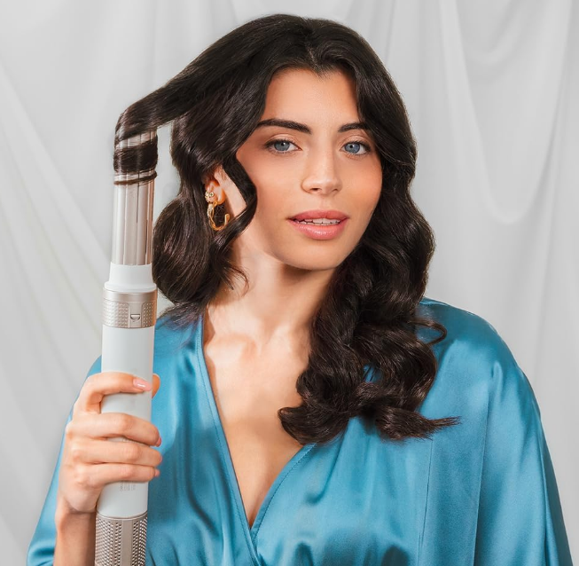 Woman using Cecotec Bamba 14in1 AirGlam Styler to curl her dark hair, wearing a blue satin robe.