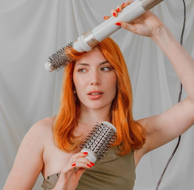 Woman styling her red hair with Cecotec Bamba 14in1 AirGlam Styler using a round brush attachment.