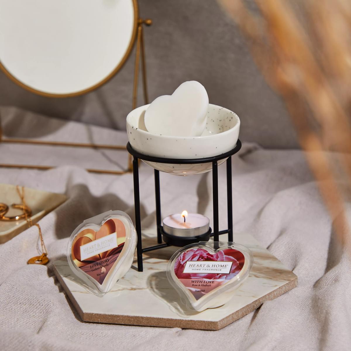 Heart-shaped Fragrance Wax Melt With Love on a ceramic warmer with lit tealight on marble tray.