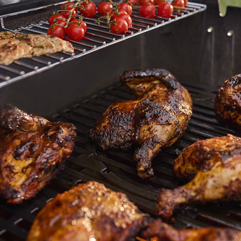Close-up of grilled chicken and cherry tomatoes cooking on the Genesis E-425W LP BLK Gas Barbecue grill.
