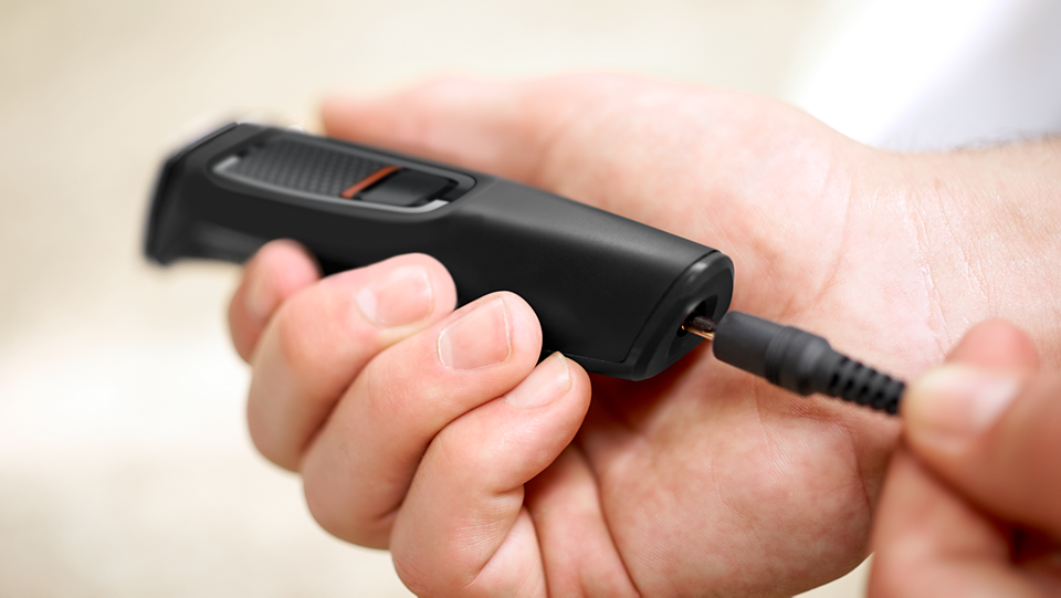 Hand holding Philips Multigroom series 3000 trimmer while plugging in the charging cable.