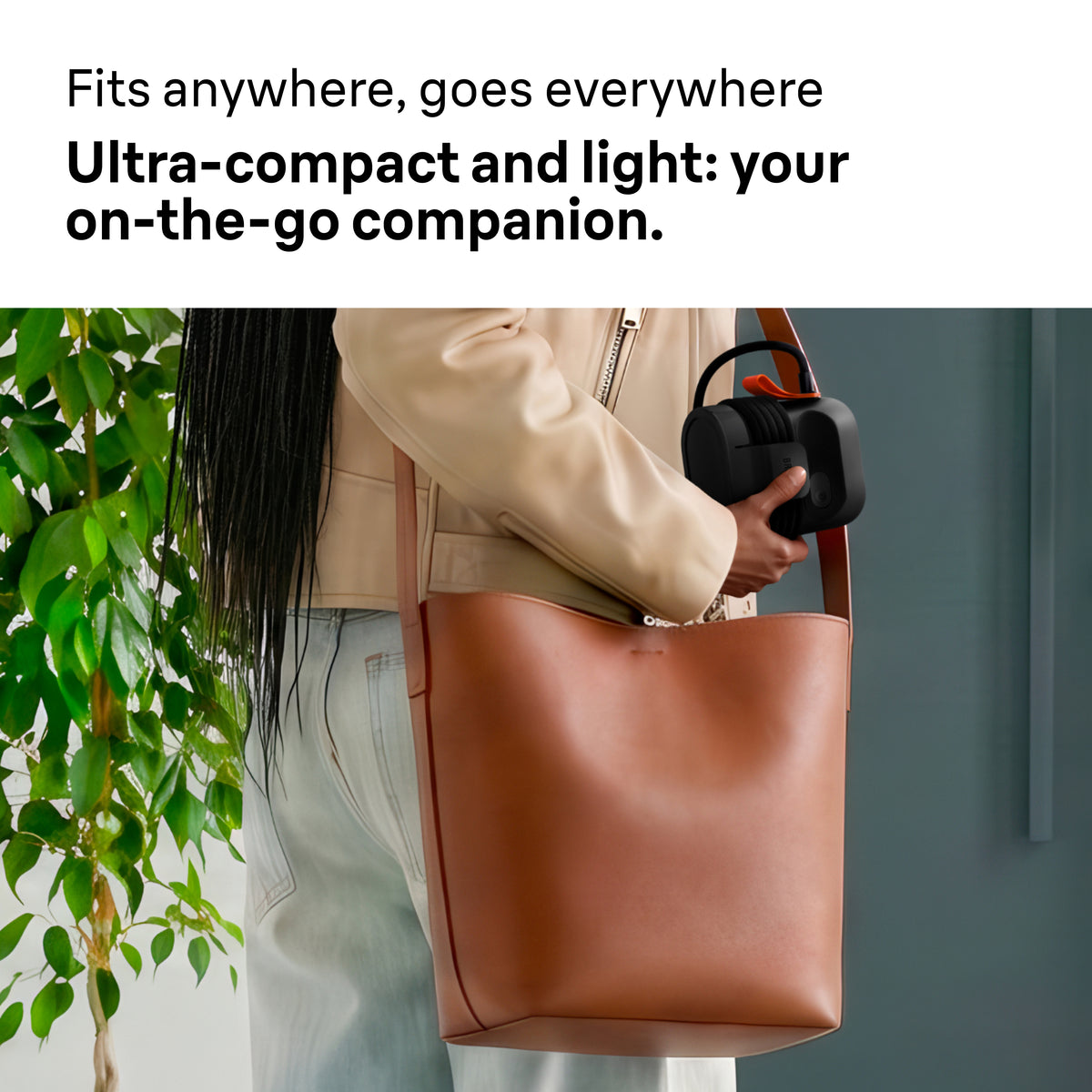 Person holding a black Braun Carestyle Mini Travel Garment Steamer with an orange handle over a brown tote bag