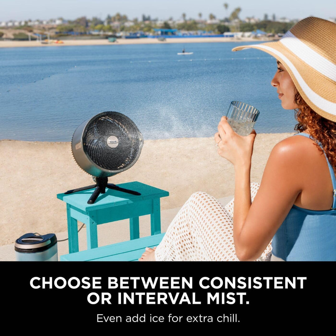 Shark FlexBreeze Pro Mist fan on a blue table misting water near a woman in a sunhat by the beach.