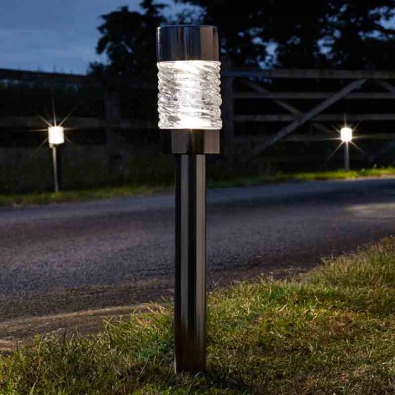 Martello Solar Nickle Stake Light glowing at night along a roadside with two more lights in the background.