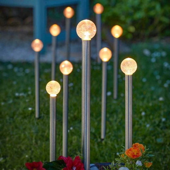 Set of 10 GlowBall Stake Lights glowing warmly in a garden at dusk among flowers and grass.