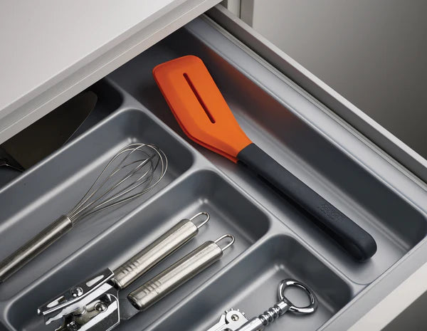 Jj Turner grey and orange tongs resting in a kitchen drawer with other utensils.