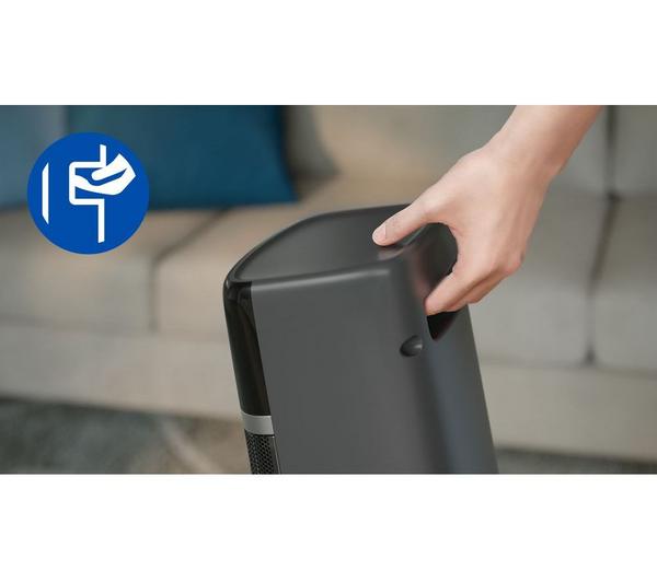 Hand holding the top handle of the dark grey Philips Smart Tower Heater 5000 Series near a sofa.
