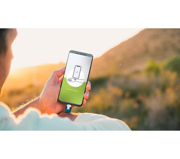 Person holding a smartphone connected to the Heat-It Classic USB C insect bite healer outdoors at sunset