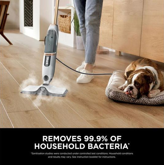 Shark SteamSpot S2001UK steam mop cleaning a wooden floor with steam visible, dog resting nearby on a bed