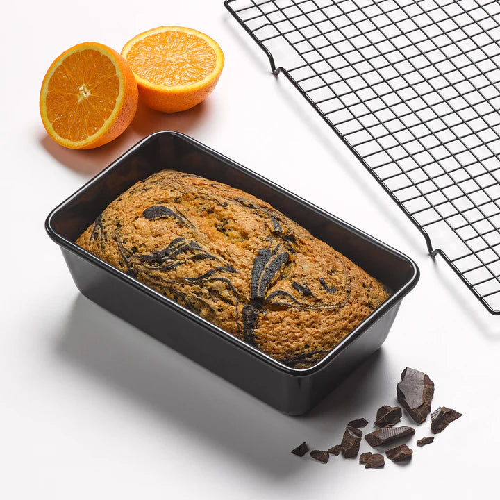 Tala Eclipse non-stick 2lb loaf tin with freshly baked chocolate swirl cake, cooling rack, orange halves, and chocolate