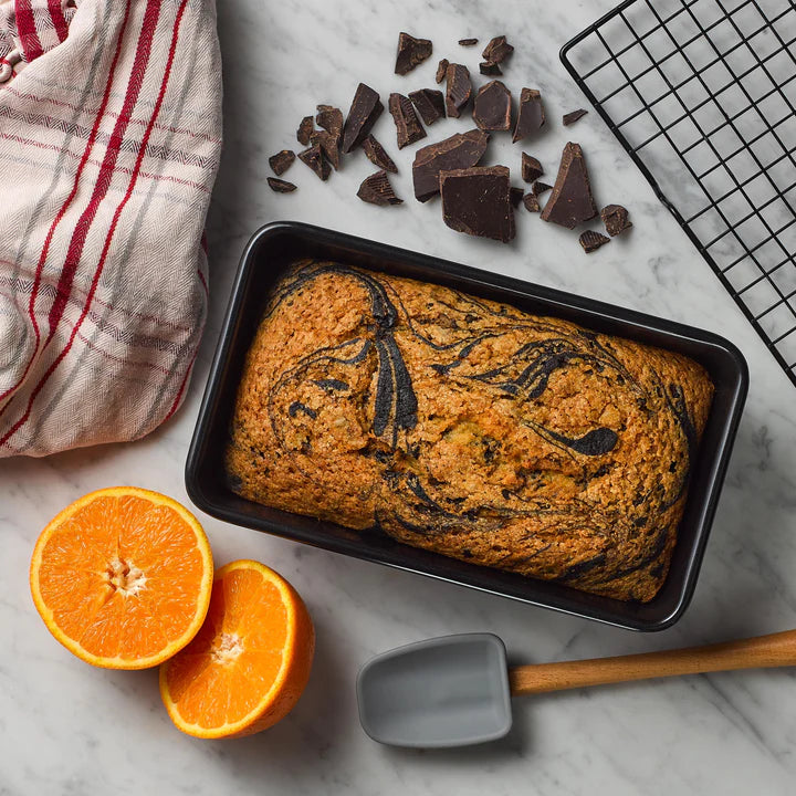 Tala Eclipse non-stick 2lb loaf tin with freshly baked marble cake on a marble surface with orange halves and chocolate