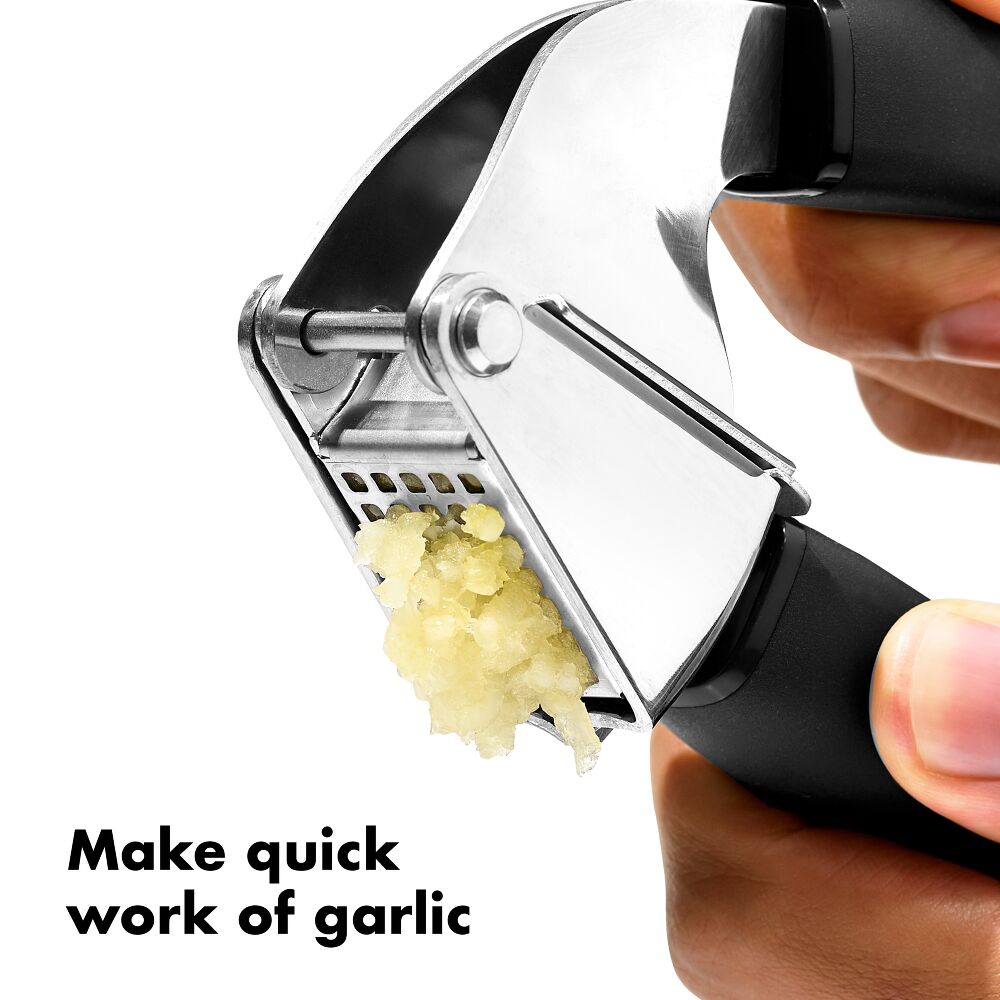 Oxo Garlic Press crushing garlic with minced garlic visible, held by hands with black handles.