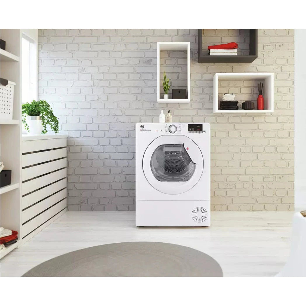 Hoover 8kg heat pump dryer in a bright laundry room with brick walls and floating shelves.