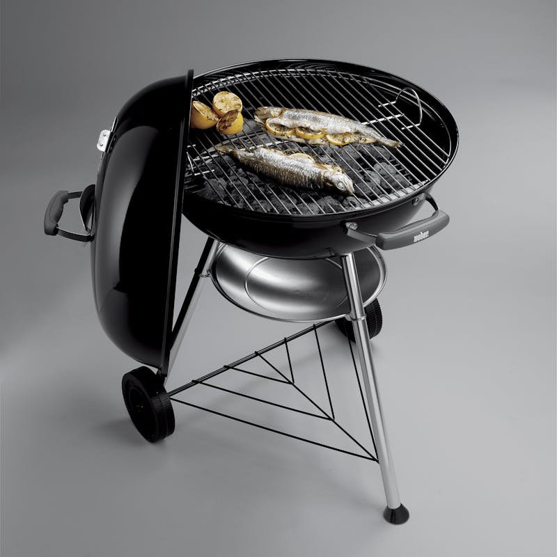 Weber Compact Kettle Charcoal Barbecue 57cm with lid open, grilling two whole fish and potatoes