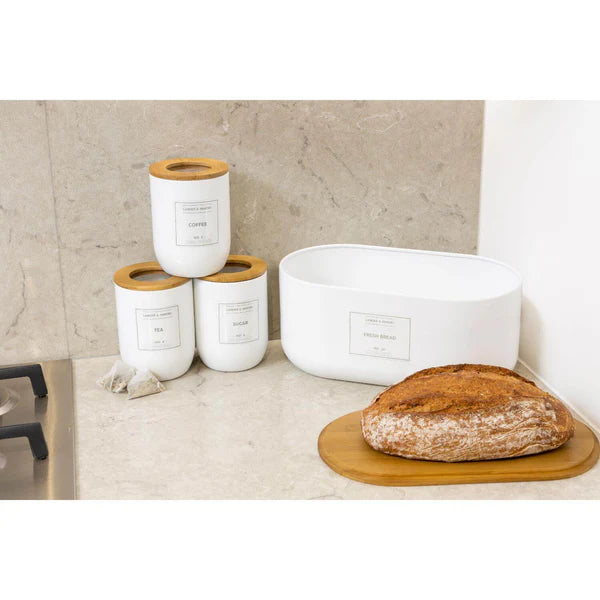 White Eden bread storage bin with label, next to matching tea, coffee, and sugar canisters on kitchen counter