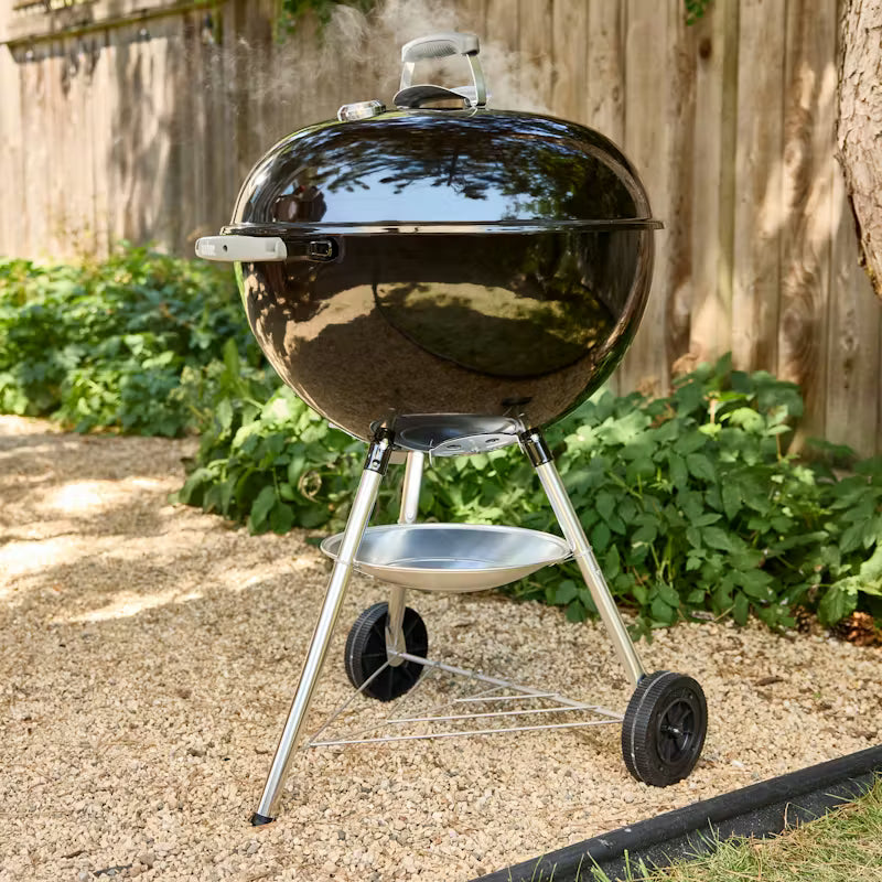 Weber Bar-B-Kettle charcoal barbecue with lid, thermometer, and wheels on gravel in garden setting