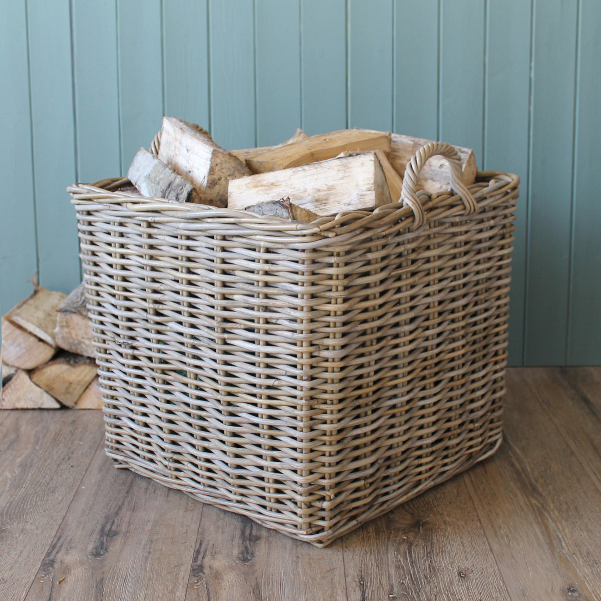 Small square Kubu wicker basket filled with firewood on wooden floor against blue wall
