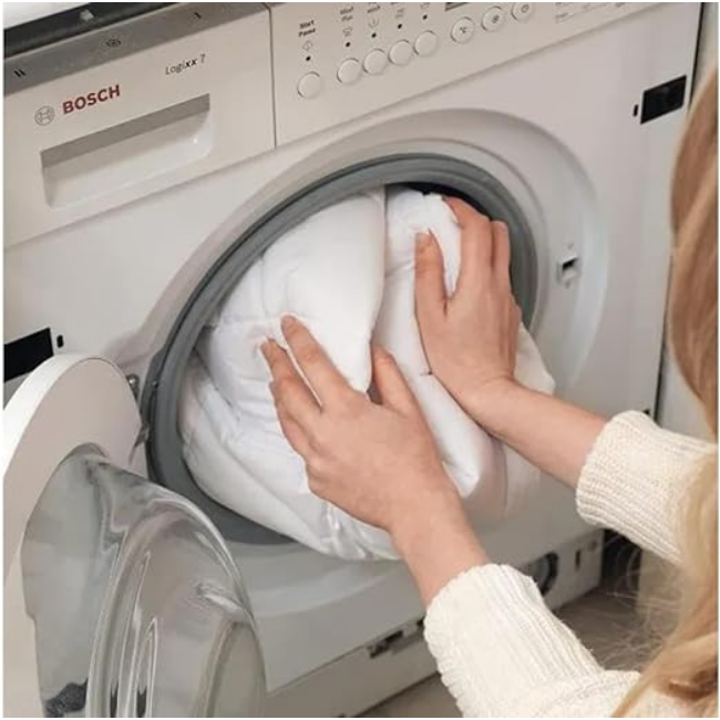 Hands placing a white Dreamland Mattress Cover Electric Blanket into a front-loading Bosch washing machine.