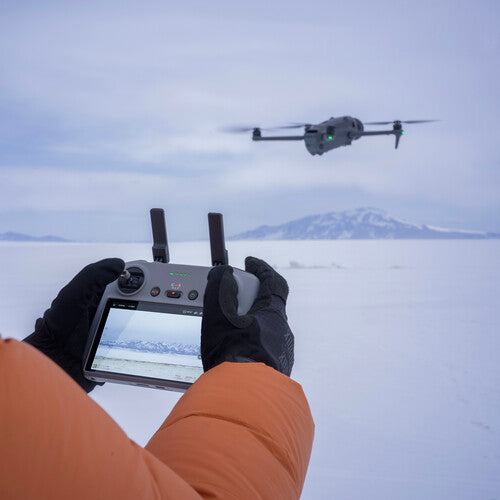 Person in orange jacket flying DJI Mavic 4 Pro drone over snowy landscape with mountains in background