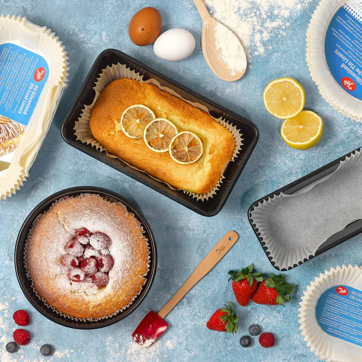 Baked lemon loaf and berry cake in Tala siliconised loaf liners with baking ingredients and empty liners on blue surface.