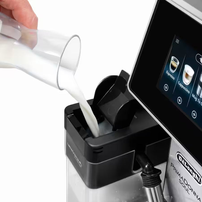Person pouring milk into a coffee machine with a PrimaDonna S900 model visible.