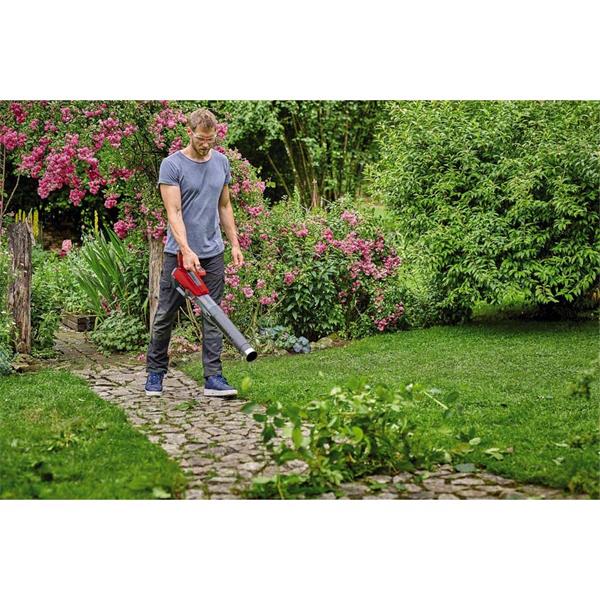 Man using red and black Einhell Power X-Change 18V cordless leaf blower on garden path with greenery and flowers