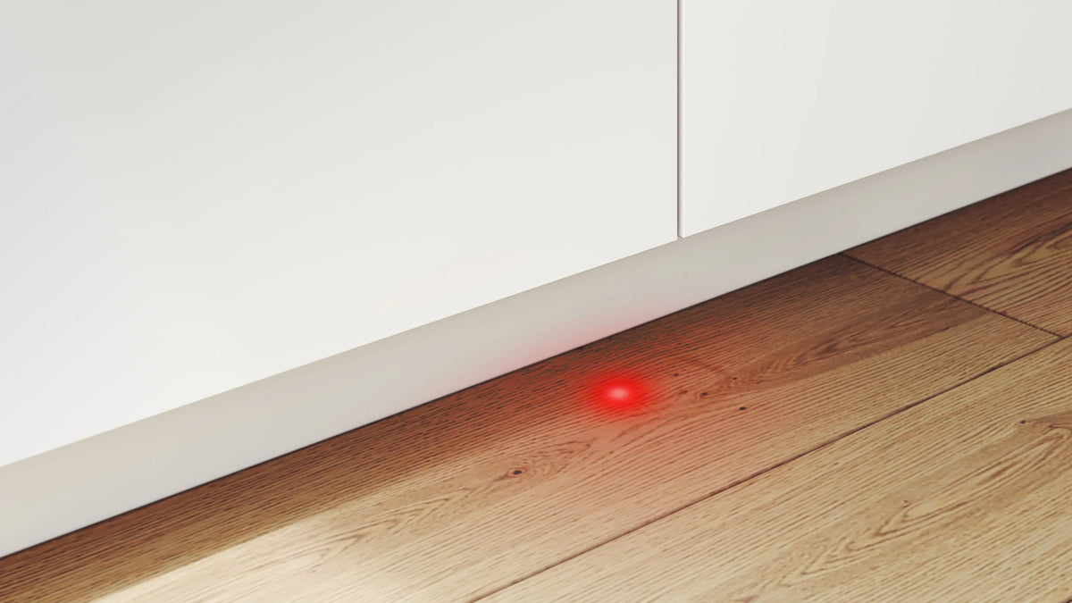 Lower section of Bosch Serie 4 fully integrated dishwasher with red light projection on wooden floor