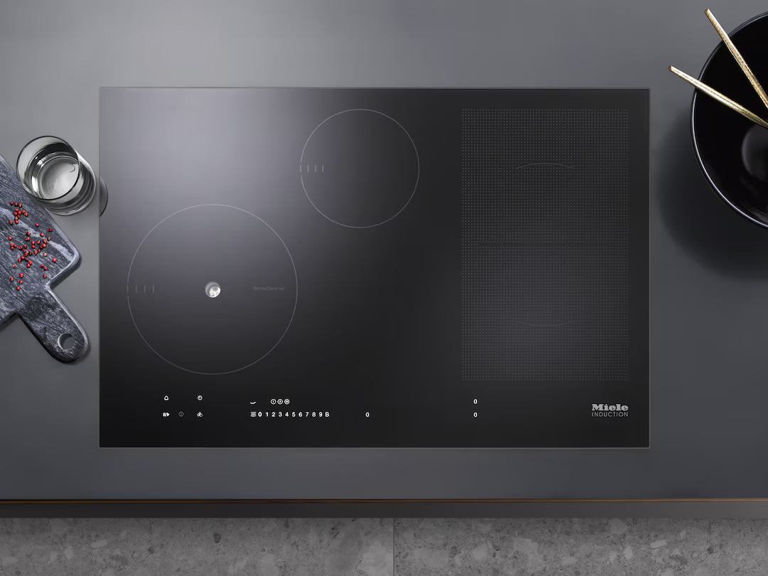 Miele KM 7699 FR 94cm black induction hob with PowerFlex zone on a grey countertop with bowl and cutting board nearby