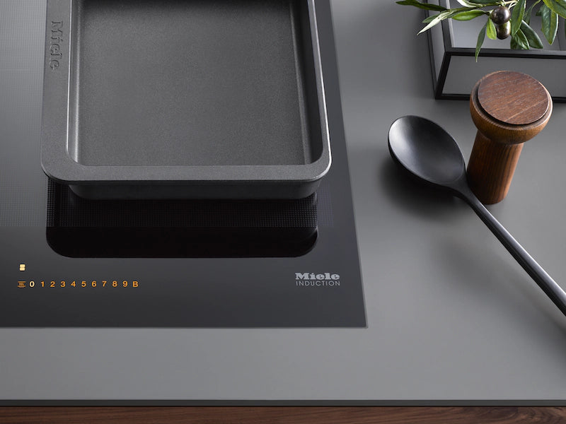 Miele KM 7474 FR induction hob with a rectangular pan on one cooking zone and control panel lit up on a grey countertop