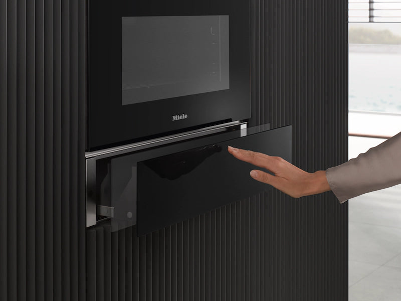 Hand opening the graphite grey Miele ESW 7020 29cm Sous Chef warming drawer built into a black kitchen wall.