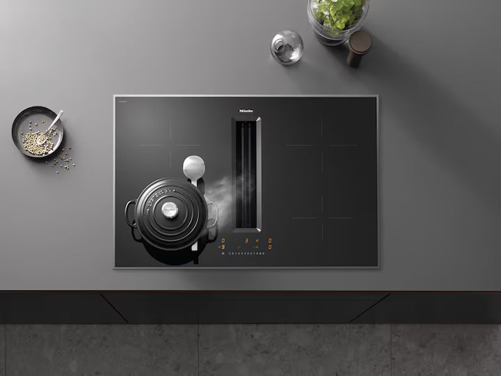 Miele induction hob with integrated vapor extractor in use, black pot steaming on left burner.
