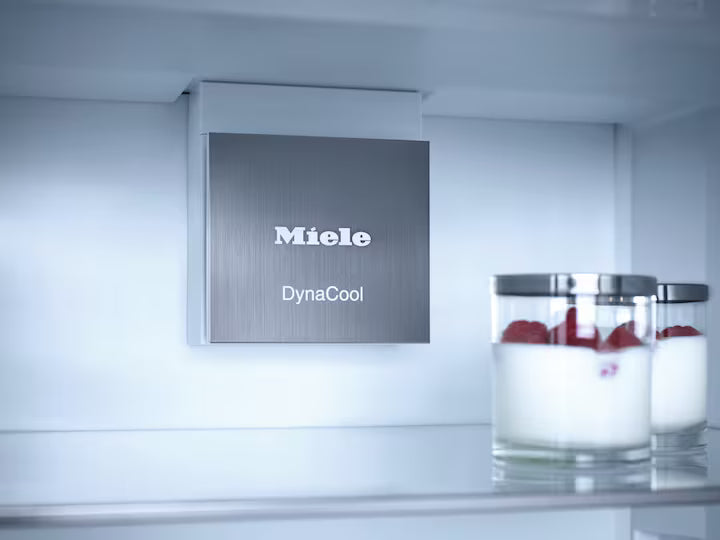 Close-up inside view of Miele K 7737 D fridge freezer showing DynaCool vent and three glasses with yogurt and raspberries.