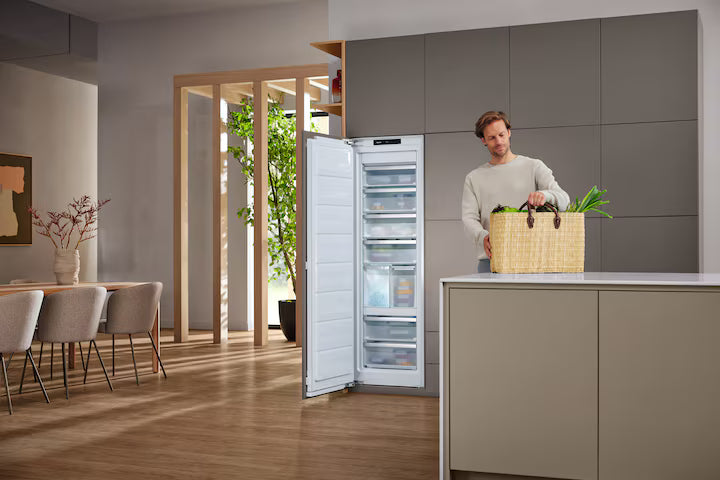 Miele FNS 7794 D upright freezer with open door showing interior drawers in modern kitchen setting
