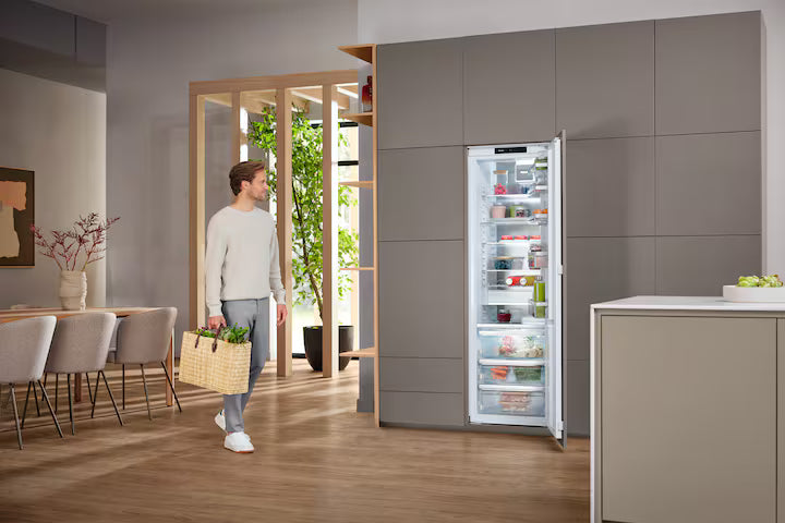 Miele K 7797 C R built-in fridge with open door showing organized fresh food inside in a modern kitchen.