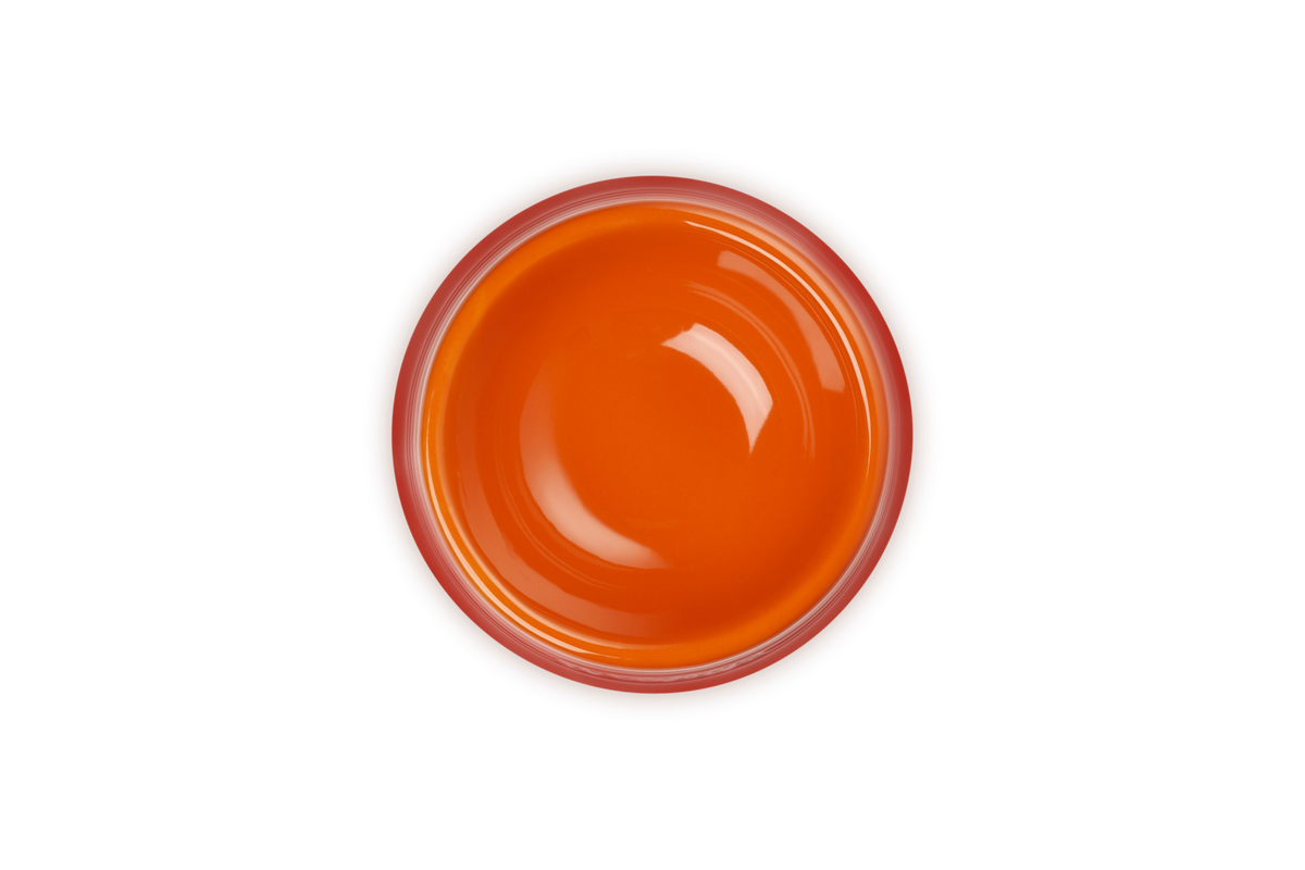 Top view of a glossy orange Le Creuset Stoneware Medium Pet Bowl in Volcanic color on a black background.