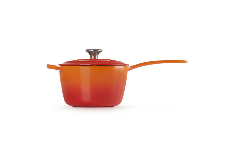 Le Creuset 20cm saucepan in volcanic orange with lid and long handle, side view on white background.