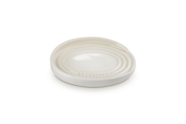 Le Creuset oval spoon rest in meringue color with concentric ring design and embossed logo.