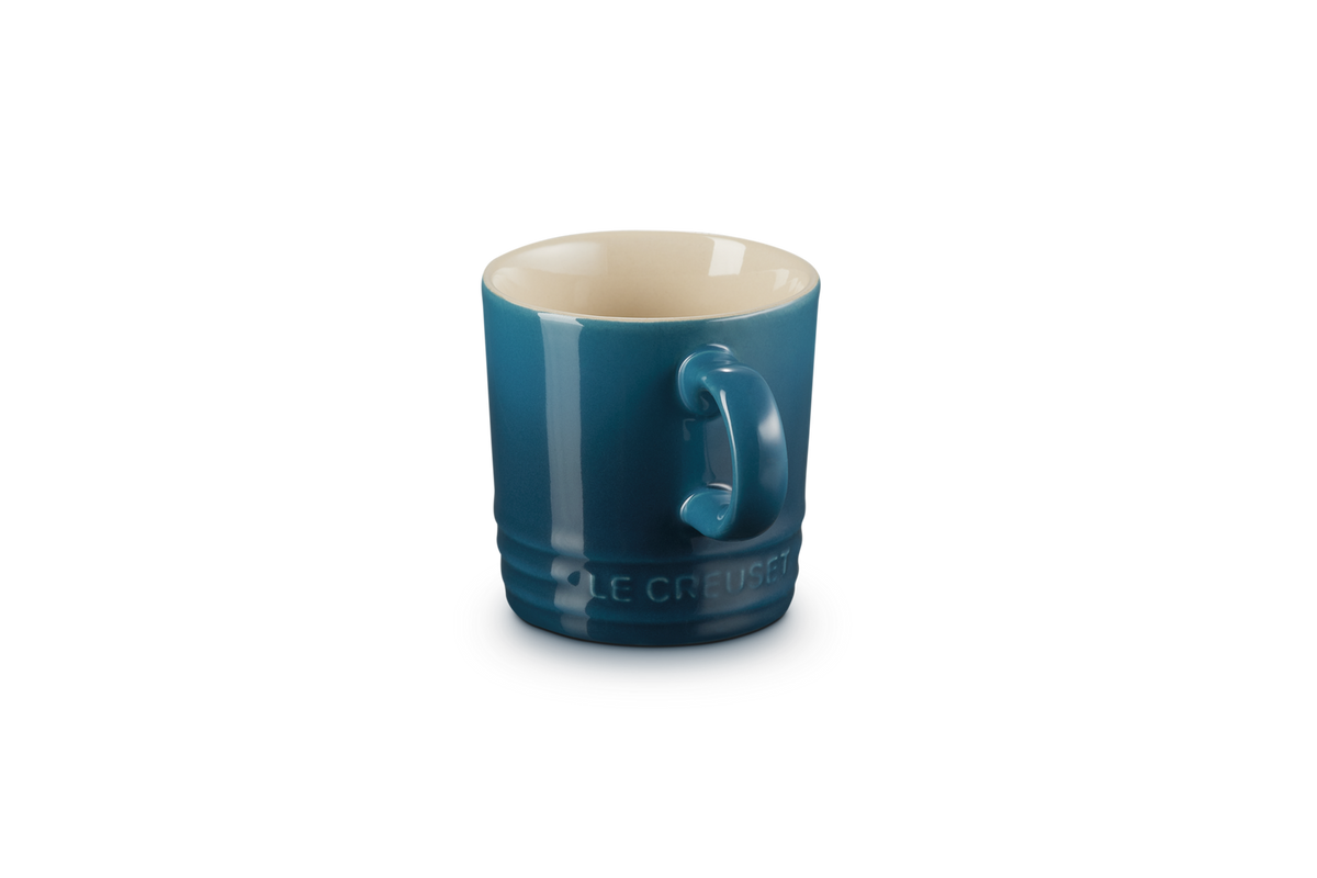 Le Creuset espresso mug in deep teal with a cream interior and embossed logo on the base.