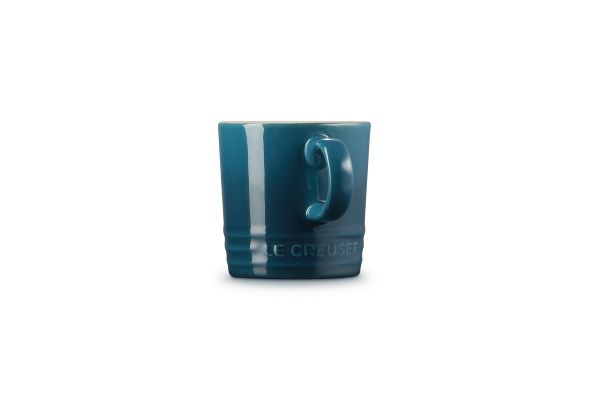 Le Creuset espresso mug in deep teal shown from the side with handle and embossed logo visible.