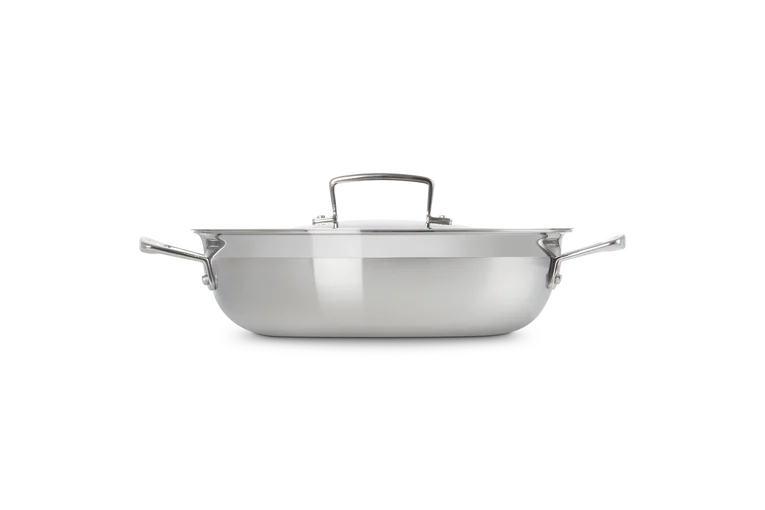 Le Creuset Classic 3-ply stainless steel shallow casserole with lid, side view on white background.