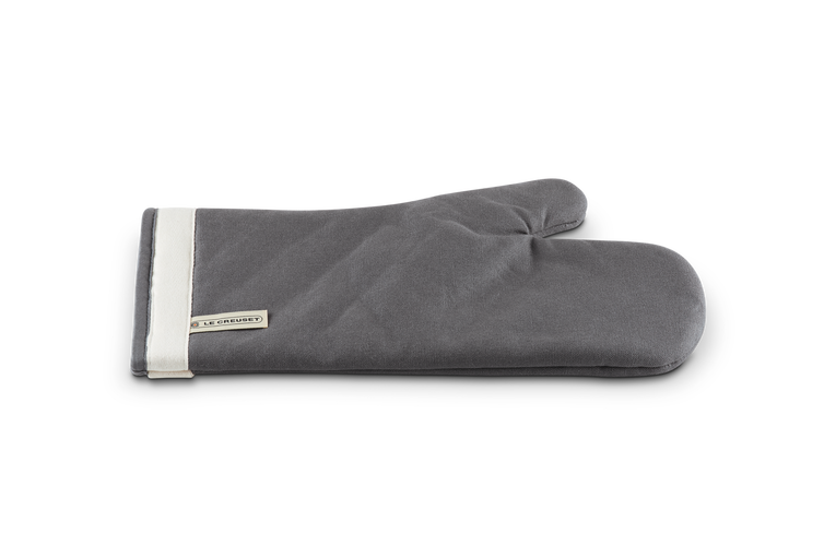 Le Creuset 14'' Flint oven mitt in gray cotton with white trim and brand label on cuff, flat lay view.
