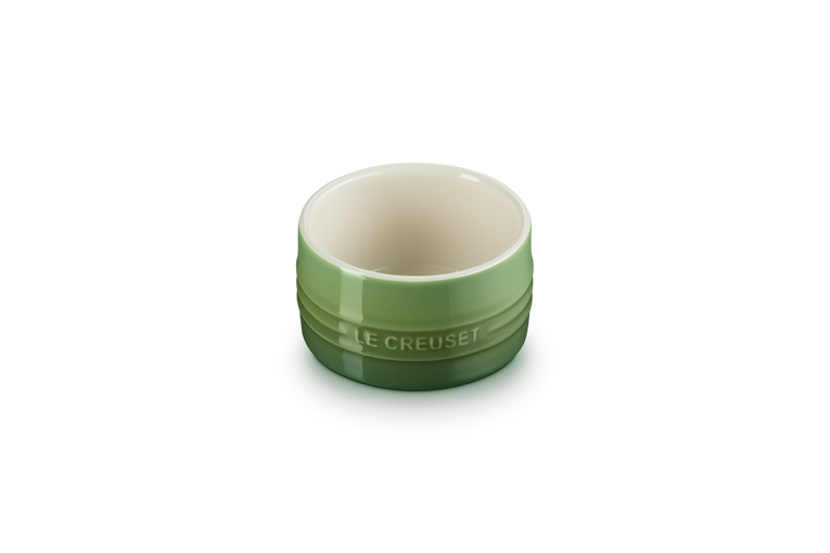 Le Creuset stackable ramekin in green with cream interior, shown from a top angle on black background.