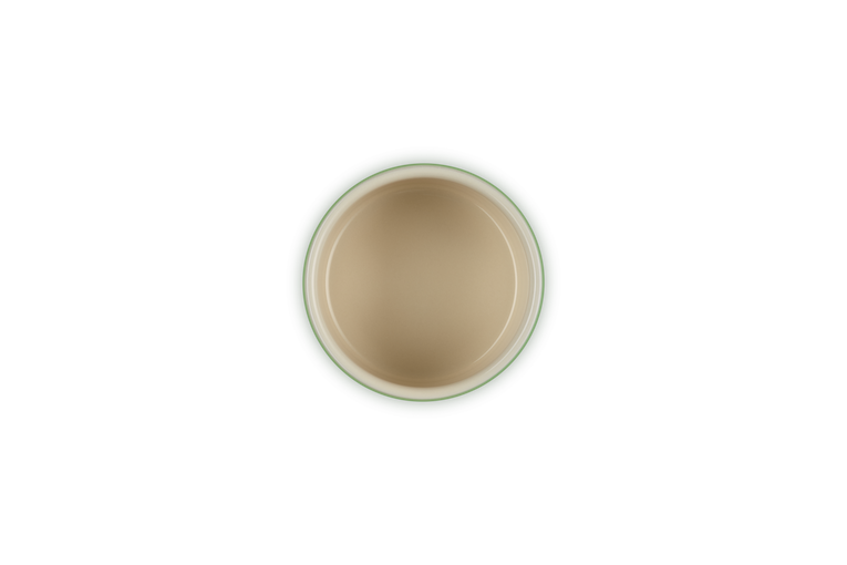 Top view of a beige Le Creuset Stackable Ramekin with a dark green rim on a black background.