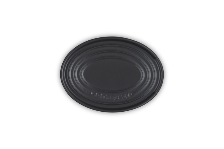 Le Creuset satin black stoneware oval spoon rest with embossed logo and concentric ridges.