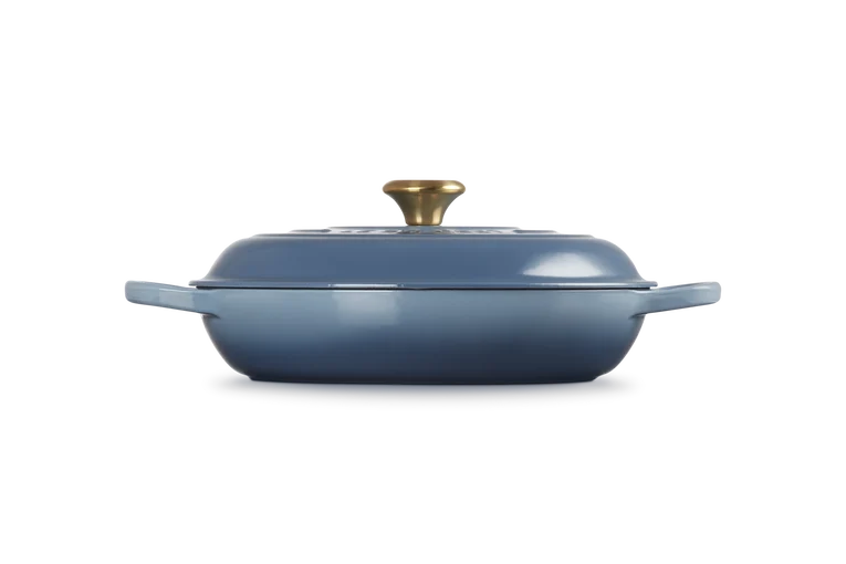 Le Creuset Signature 30cm shallow cast iron casserole in chambray blue with gold knob lid, side view.