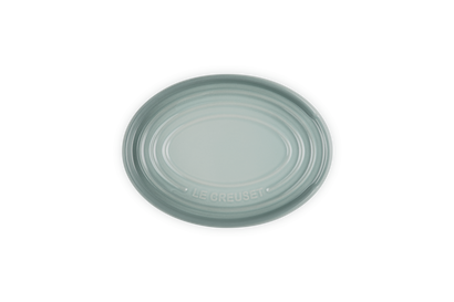 Le Creuset oval stoneware spoon rest in sea salt color with concentric ridges and logo embossed.