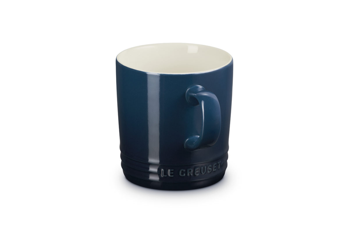 Le Creuset London Mug 350ml in deep blue with cream interior, handle visible, embossed logo near base.