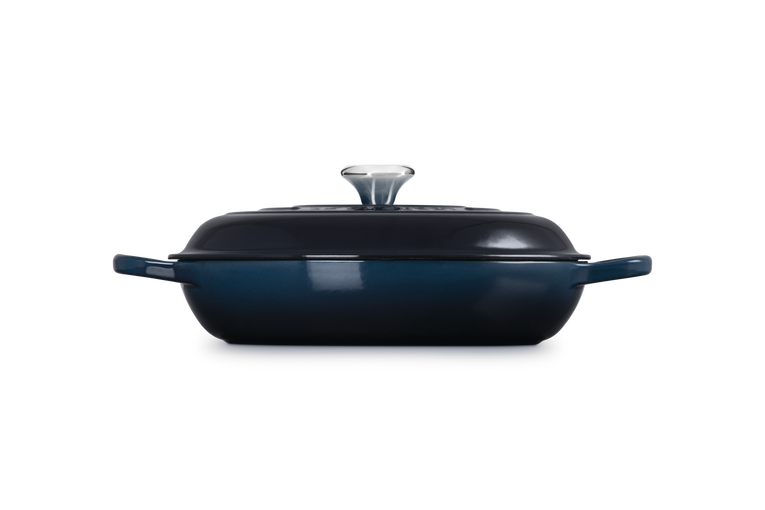 Le Creuset 30cm shallow cast iron casserole in deep blue with lid and silver knob, side view.